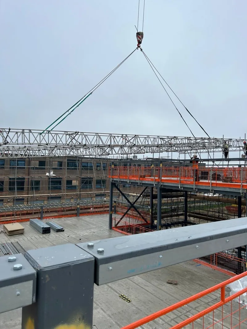 Mobile crane lifting a lattice-beam roof truss onto the support scaffold above the steel frame